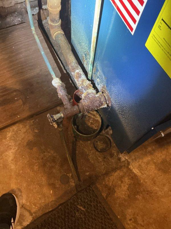 Responded to a reported leak at the boiler piping and found severe corrosion and mineral buildup at the boiler's drain/valve tee and associated fittings, indicating long-term seepage. Inspected the affected piping and connections, documented the condition, and addressed the leak at the corroded joints to stop active leakage, with the remaining corroded piping noted for monitoring and potential replacement.