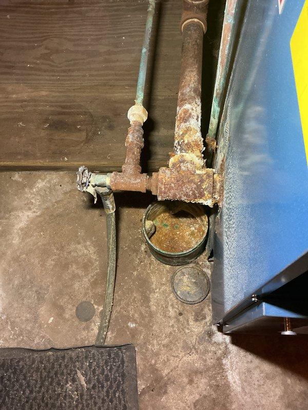 Responded to a reported leak at the boiler piping and found severe corrosion and mineral buildup at the boiler's drain/valve tee and associated fittings, indicating long-term seepage. Inspected the affected piping and connections, documented the condition, and addressed the leak at the corroded joints to stop active leakage, with the remaining corroded piping noted for monitoring and potential replacement.