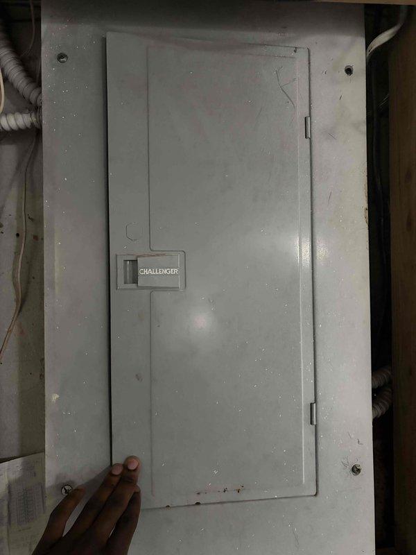 Inspected the main electrical service panel and surrounding wiring as part of an assessment for a tripped circuit breaker and a non-operational AC system. Examined the panel cover, hardware, and conduit, noting surface rust along the lower edge of the panel door and dust accumulation. Documented panel condition and adjacent service components with photos to support evaluation of whether repair or system replacement is warranted.