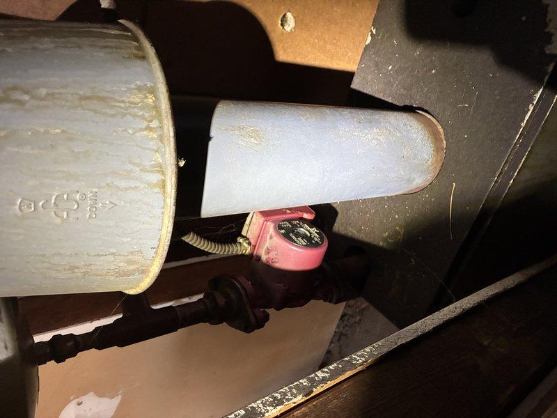 Responded to a no-heat complaint on a radiant floor system and inspected the boiler, circulator pump, flue venting, and associated piping and electrical connections in the mechanical area. Documented corrosion, staining, and weathering on the boiler cabinet and flue components, along with aged circulator piping, and evaluated system operation to diagnose why the radiant loop was not delivering heat to the floors.
