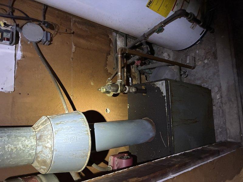 Responded to a no-heat complaint on a radiant floor system and inspected the boiler, circulator pump, flue venting, and associated piping and electrical connections in the mechanical area. Documented corrosion, staining, and weathering on the boiler cabinet and flue components, along with aged circulator piping, and evaluated system operation to diagnose why the radiant loop was not delivering heat to the floors.