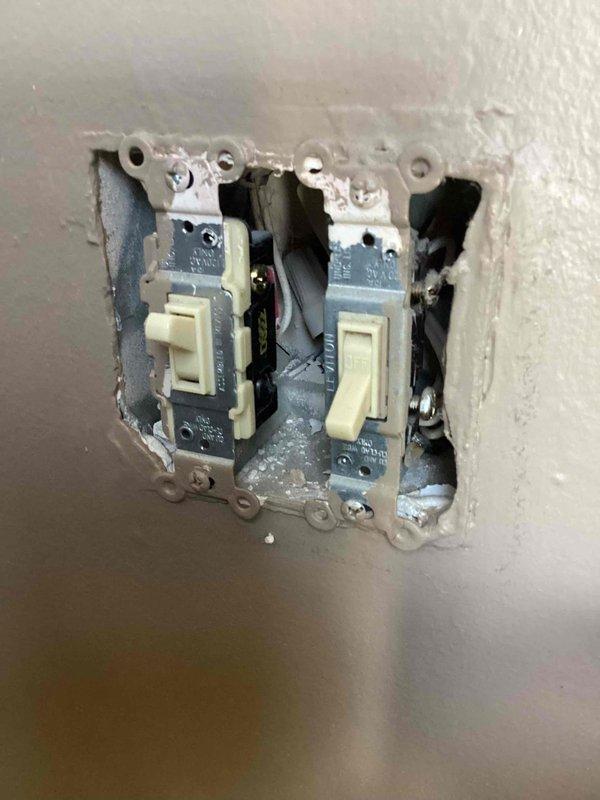 Performed an electrical inspection of the residence, including a visual examination of a double-gang switch assembly and a kitchen backsplash duplex receptacle. The two Leviton toggle switches were found mounted in a ragged, oversized drywall opening with paint and joint compound buildup on the mounting straps and no cover plate installed, while the kitchen receptacle showed no signs of damage, overheating, or abnormal conditions under normal appliance loading. The switch cutout is recommended for drywall repair and installation of a cover plate to ensure proper protection and code-compliant finish.