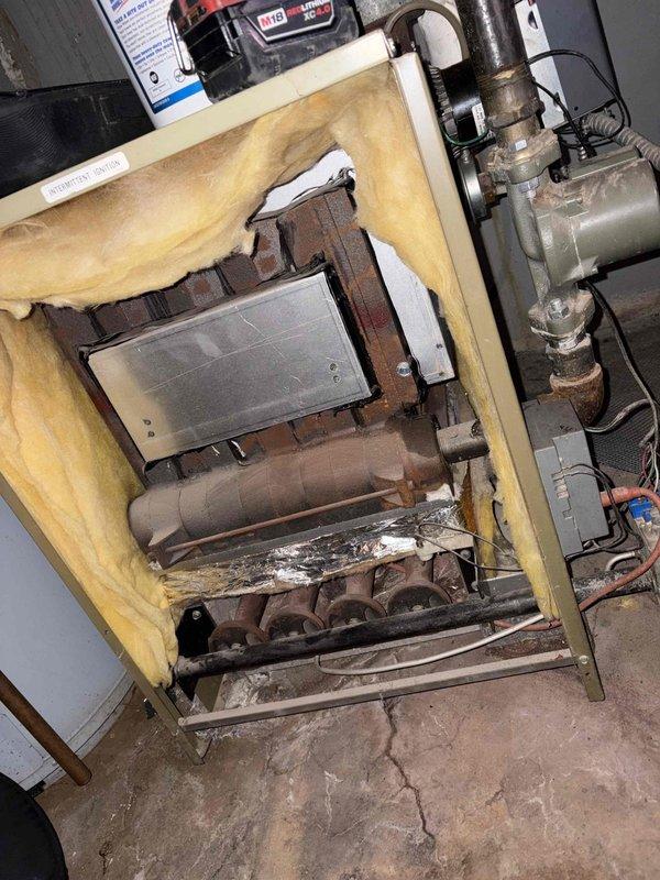 Performed a heating tune-up on a single gas-fired boiler/furnace unit (10+ years old), including removal of the front cover panel and inspection of the combustion chamber, burner assembly, circulator pump, and controls. Observed ignition and burner flame operation, noting blue flame characteristics with some orange tipping. Identified significant corrosion on burner components and a rusted baffle/heat exchanger section, torn and deteriorated cabinet insulation, aged refractory brickwork, and heavy rust on the circulator piping, and documented all findings with photos for recommended follow-up evaluation.