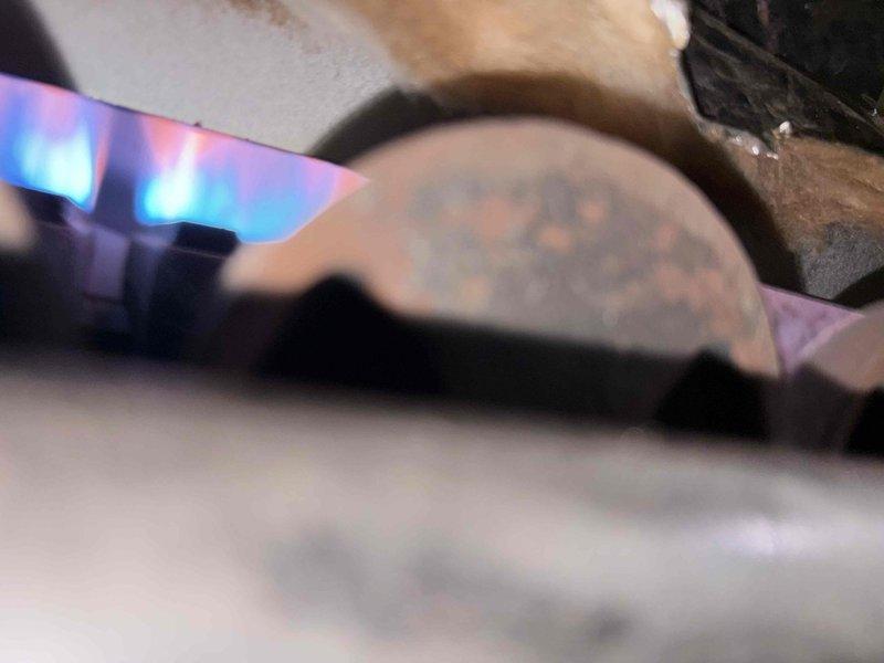 Performed a heating tune-up on a single gas-fired boiler/furnace unit (10+ years old), including removal of the front cover panel and inspection of the combustion chamber, burner assembly, circulator pump, and controls. Observed ignition and burner flame operation, noting blue flame characteristics with some orange tipping. Identified significant corrosion on burner components and a rusted baffle/heat exchanger section, torn and deteriorated cabinet insulation, aged refractory brickwork, and heavy rust on the circulator piping, and documented all findings with photos for recommended follow-up evaluation.