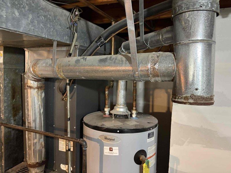Performed a no-heat diagnostic inspection, including a visual check of the heat exchanger for cracks and an evaluation of the flame rollout switches. During the inspection, the galvanized flue/vent connector above the water heater was found to have heavy rust and corrosion along its lower edge and a pinhole perforation in the pipe wall, which presents a flue gas leakage and carbon monoxide risk. Recommend replacement of the corroded vent connector and re-inspection of the venting system for proper draft and sealing.