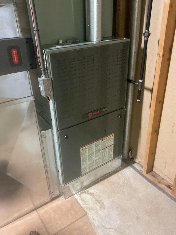 Performed annual heating tune-up on a Trane gas furnace with an attached Trane humidifier, inspecting the cabinet, flue vent, gas piping, electrical junction, and ductwork connections. System was confirmed operating properly at time of service, with no rust, frost, or equipment damage observed; a damp stained area was noted on the concrete floor near the base of the furnace and should be monitored.