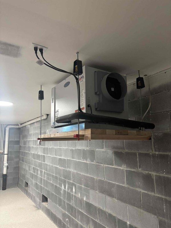 Completed HVAC system assessment of mechanical room installation. Documented existing air handler unit mounted on wall-mounted shelf system with associated ductwork and electrical connections, as well as basement-level flex duct distribution system requiring proper tensioning and securing of loosely draped sections to meet code compliance standards.