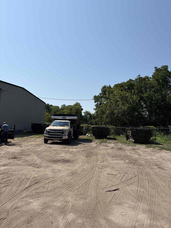 Completed site assessment for new 50-amp electrical service installation at commercial facility. The proposed service run measures approximately 65 feet from the existing customer service entrance disconnect (CSED) to the main building, requiring conduit routing across an exterior dirt lot area. Documented existing electrical infrastructure including weatherhead assembly, vertical conduit penetration through corrugated metal siding, and current panel configuration to determine material requirements and installation methodology for the new circuit.
