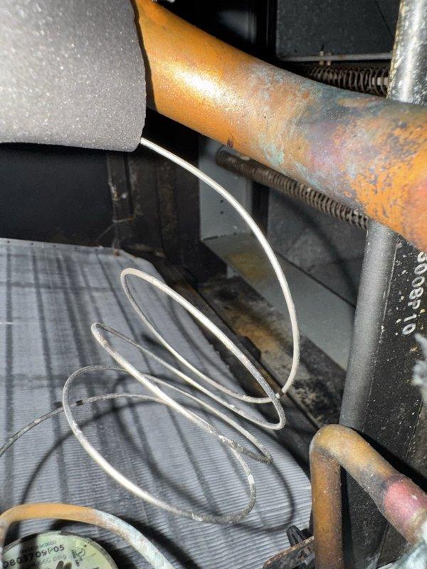 Responded to service call for non-functioning Nest thermostat with blank display and no baseplate illumination. Upon inspection, accessed HVAC system interior and found heavily dust-contaminated compartment with aged wiring bundle showing wear. Inspected thermostat control wiring consisting of multiple colored conductors (red, yellow, white, and black) with visible dust accumulation and aging throughout the system. Examined related HVAC components including corroded copper refrigerant line with significant oxidation, heat exchanger coils, and associated mechanical elements within the unit housing. Documented system condition showing extensive dust buildup on all interior surfaces and compartment panels, indicating need for comprehensive system maintenance beyond the immediate thermostat power issue.