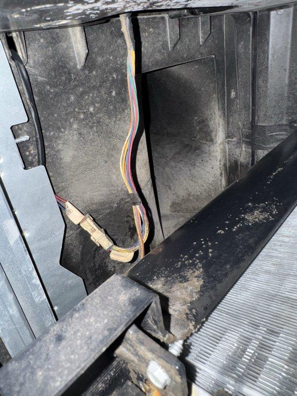 Responded to service call for non-functioning Nest thermostat with blank display and no baseplate illumination. Upon inspection, accessed HVAC system interior and found heavily dust-contaminated compartment with aged wiring bundle showing wear. Inspected thermostat control wiring consisting of multiple colored conductors (red, yellow, white, and black) with visible dust accumulation and aging throughout the system. Examined related HVAC components including corroded copper refrigerant line with significant oxidation, heat exchanger coils, and associated mechanical elements within the unit housing. Documented system condition showing extensive dust buildup on all interior surfaces and compartment panels, indicating need for comprehensive system maintenance beyond the immediate thermostat power issue.
