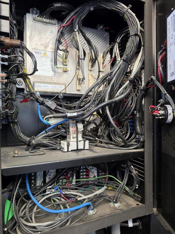 Conducted comprehensive inspection of building's backup generator system per customer request. Documented current condition of generator control panel and electrical components, including extensive wiring configurations, control modules, and terminal connections. Photographed interior of electrical cabinet showing upper and lower shelf arrangements with white control box, multiple cable bundles, and various colored wiring throughout system. Noted handwritten operational reference notes on wall indicating generator start sequence and component identifiers. Assessment completed to provide maintenance recommendations and identify any necessary repairs to ensure reliable generator operation.