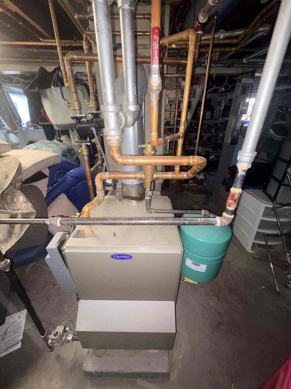 Diagnosed a leaking cast iron baseboard radiator on the second floor, which was installed in sections with a failed connection at the seam. Confirmed isolation valves for the zone, documented the leak location with photos, and recorded equipment information including the Carrier heating system located in the basement mechanical area.