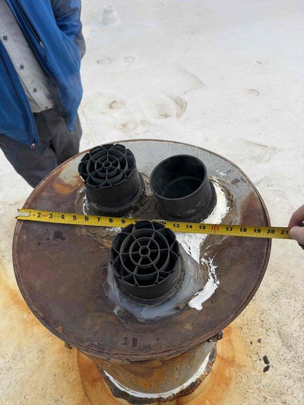 Responded to service call for water leakage affecting two top-floor units. Inspected rooftop drainage components, identified corroded circular metal fitting with visible rust and white residue. Measured component diameter (18-21 inches) and documented condition of three black cylindrical fittings with compromised honeycomb structure that were contributing to the water infiltration issue.