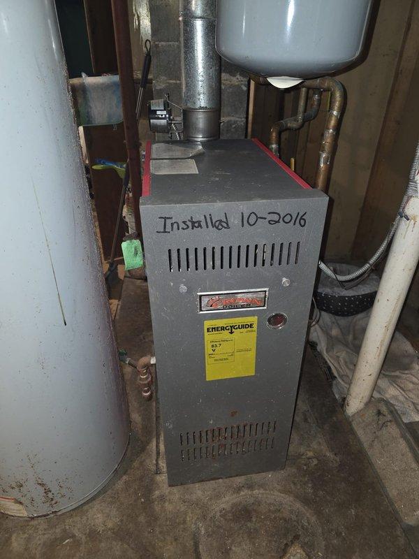 Performed estimate for replacement of vintage-style column radiator in residential setting. Current radiator (white/cream with wooden top panel) requires replacement per previous assessment. Noted existing HVAC system includes furnace installed in 2016 with connected copper piping and ventilation components.