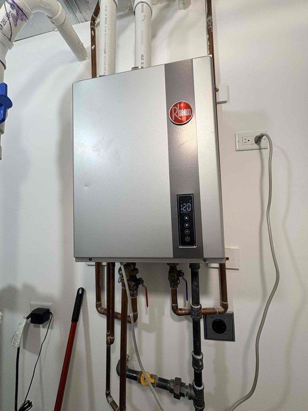 Diagnosed and documented water leak at the wall penetration of the exhaust pipe on a Rheem tankless water heater system. Observed damaged wall surface and improper sealing around the 2" PVC exhaust pipe where it enters the wall. Photos taken of the installation and leak area for documentation and repair quote purposes. Customer advised of recommended repairs and maintenance options for both water heater and furnace systems.