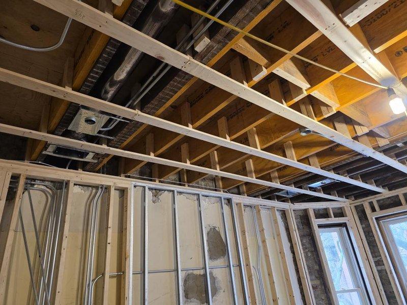 Conducted HVAC rough-in inspection of the installation progress. Verified proper placement of ductwork and ventilation components between ceiling joists and confirmed appropriate clearances for the system. Documented the current construction phase with photographs showing exposed framing, utility systems, and Delta-M vapor barrier installation prior to drywall application.