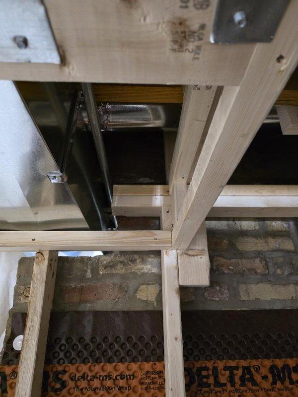 Conducted HVAC rough-in inspection of the installation progress. Verified proper placement of ductwork and ventilation components between ceiling joists and confirmed appropriate clearances for the system. Documented the current construction phase with photographs showing exposed framing, utility systems, and Delta-M vapor barrier installation prior to drywall application.