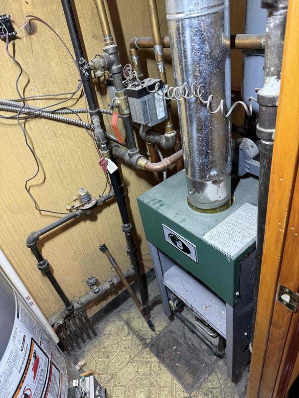 Performed annual boiler clean and check service on residential heating system. Inspected copper piping network, valves, zone control devices, and green boiler unit with exhaust venting. System shows normal aging but remains in functional operating condition with no immediate issues requiring repair.
