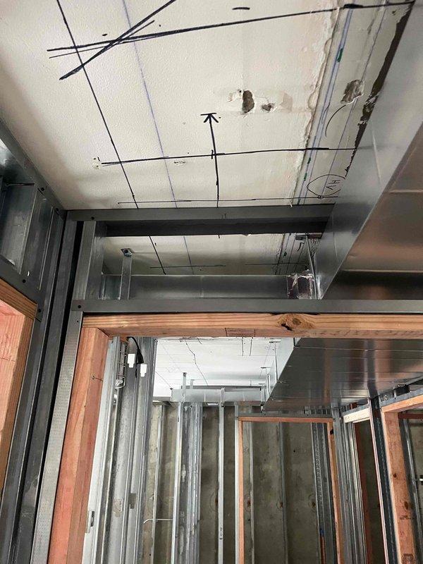 Continued commercial ductwork installation in interior construction phase. Installed large curved metal air duct runs along ceiling area, coordinating with existing metal stud framing. Work included integration with electrical pathways and preparation for upcoming phases around doorway openings and corridor sections.