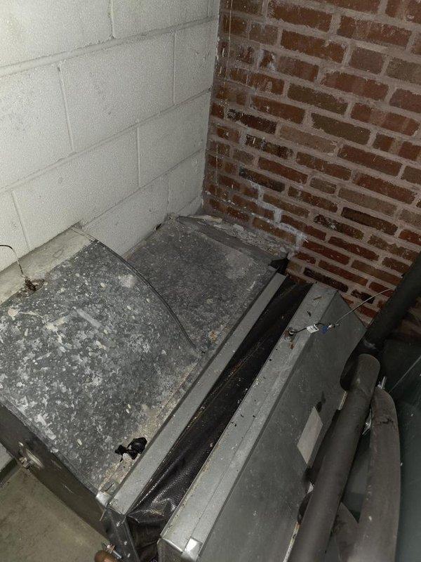 Conducted full system assessment of commercial HVAC unit located in utility room showing significant dust accumulation and requiring maintenance. Evaluation included inspection of equipment positioning against block/brick wall junction and associated ductwork. Noted conference room served by system requires adequate climate control for occupant comfort during meetings.