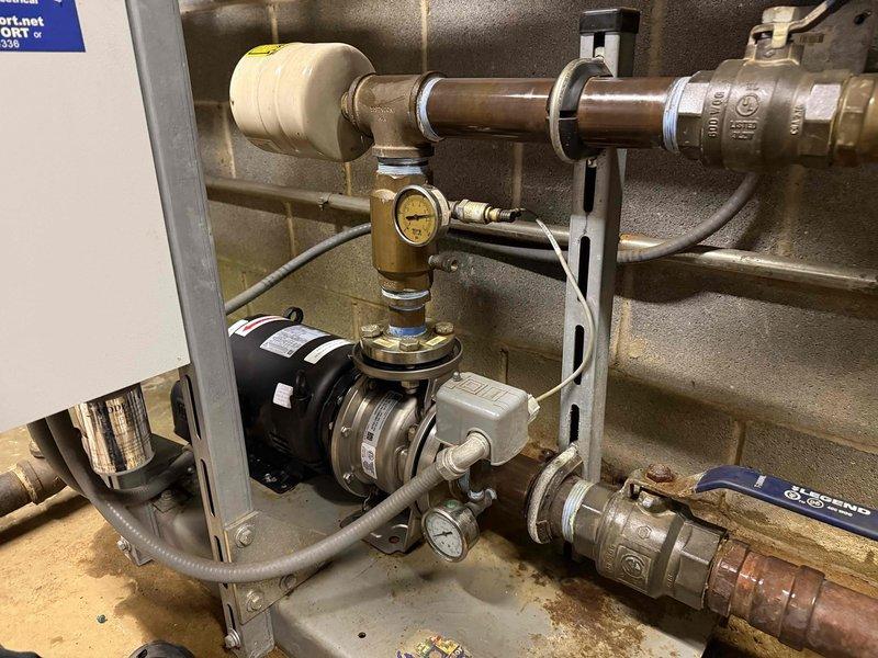 Replaced failed booster pump motor and bearing assembly on commercial HVAC system. System was dismounted from concrete block wall mounting, new components were installed with proper fittings, and system was pressure tested for proper operation before returning to service.