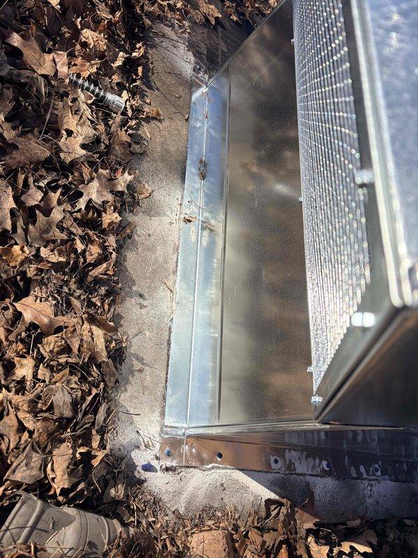 # Service Summary

Installed custom fabricated air intake hood over existing steel grate at boiler intake piping location to provide weather protection and improve system efficiency.

# Work Performed

Responded to commercial facility for installation of protective air intake hood assembly at boiler system intake point. Upon arrival, located existing steel grate where boiler intake piping penetrates building foundation at exterior wall. 

Fabricated and installed galvanized steel barrel-vault style hood enclosure to cover and protect the intake grate opening. Hood features rounded cylindrical top section transitioning to flat vertical side panels, providing complete weather protection while maintaining proper airflow to boiler intake system. Secured metal enclosure to brick exterior wall and foundation using appropriate fasteners for masonry application.

Ensured proper clearances around existing black conduit piping running vertically along brick wall. Verified hood installation does 