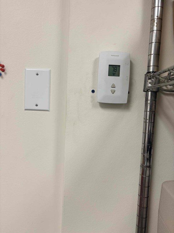 Responded to service call for non-operational air conditioning unit serving computer server room. Upon arrival, verified thermostat reading of 78°F and inspected Honeywell digital control mounted in mechanical room. Proceeded to rooftop to assess outdoor condensing unit condition. Performed visual inspection of rooftop-mounted condenser unit, noting equipment location on gravel surface with proper base pad installation. Documented system components including fan assembly, louvered cabinet, and surrounding HVAC infrastructure. Completed initial diagnostics within standard service timeframe and coordinated with office regarding additional diagnostic requirements and approval process for continued troubleshooting. Photographed thermostat display, wall-mounted controls, and exterior condensing unit for service documentation.