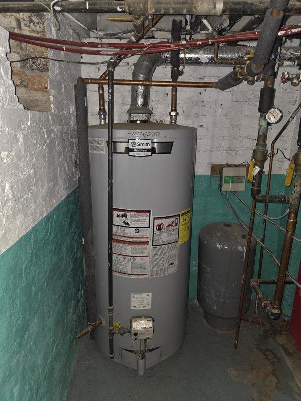 Conducted comprehensive assessment of existing HVAC and hydronic heating system for planned residential renovation project. Evaluated current basement mechanical room containing water heater, expansion tank, and complex piping network including copper, black insulated, and color-coded distribution lines with multiple valves and gauges. Documented existing two-tone painted mechanical space with overhead piping infrastructure and window access. Reviewed architectural plans specifying retention of select radiators while replacing others with baseboard units. Assessed feasibility of installing new combination hot water/boiler system in basement to serve primary heating zones. Evaluated existing R410A outdoor compressor unit for compatibility and potential reuse with planned Space-Pak high-velocity air conditioning system to be installed in attic location near current equipment. Confirmed separate inline water heater specification for two new attic bathroom additions independent of main hea