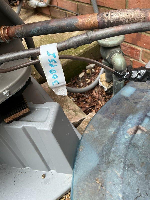 Completed ISO test and pressure recheck on outdoor HVAC lineset showing visible corrosion and oxidation on copper piping. Documented condition of exterior mechanical components, including weathered metal surfaces and junction box assemblies, to assess potential leak source and determine lineset routing and length specifications for warranty evaluation.
