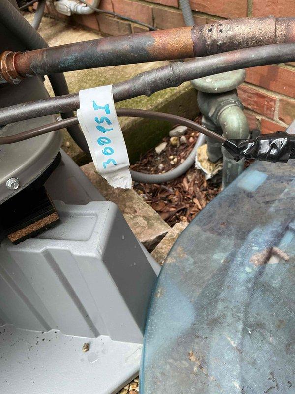 Completed ISO test and pressure recheck on outdoor HVAC lineset showing visible corrosion and oxidation on copper piping. Documented condition of exterior mechanical components, including weathered metal surfaces and junction box assemblies, to assess potential leak source and determine lineset routing and length specifications for warranty evaluation.