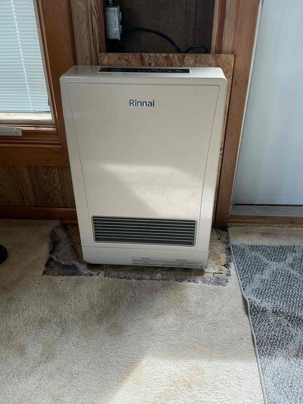 Completed installation of Rinnai furnace unit in residential setting after retrieving necessary part from office. Unit was successfully positioned in wooden alcove, connected to power supply and ventilation system, and fully commissioned with all operational checks verified.
