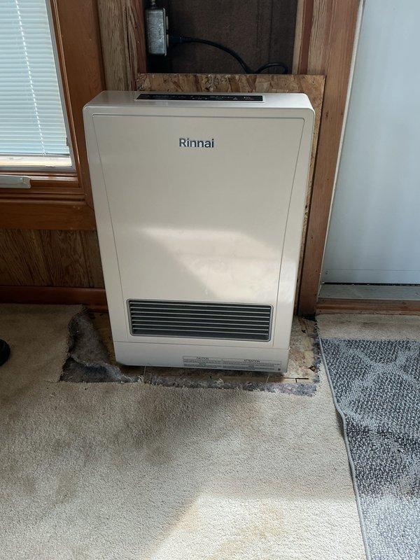 Completed installation of Rinnai furnace unit in residential setting after retrieving necessary part from office. Unit was successfully positioned in wooden alcove, connected to power supply and ventilation system, and fully commissioned with all operational checks verified.
