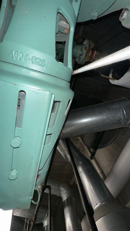 Responded to service request to document bearing condition on HVAC equipment unit 1304-028. Photographed turquoise-painted mechanical housing showing visible wear, rust staining at seams and joints, and associated piping system with insulated sections for maintenance records and assessment purposes.