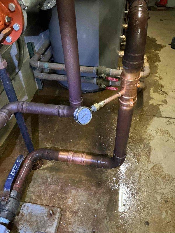 Installed pressure monitoring system on booster pump assembly by adding tee fitting with gauge on 2" inlet side. Replaced defective pressure gauge at booster pump location and installed new gauge near expansion tank downstream. Addressed water leak concerns in mechanical room where evidence of moisture and water staining was present on concrete floor beneath copper piping system with oxidized connections and multiple ball valves.