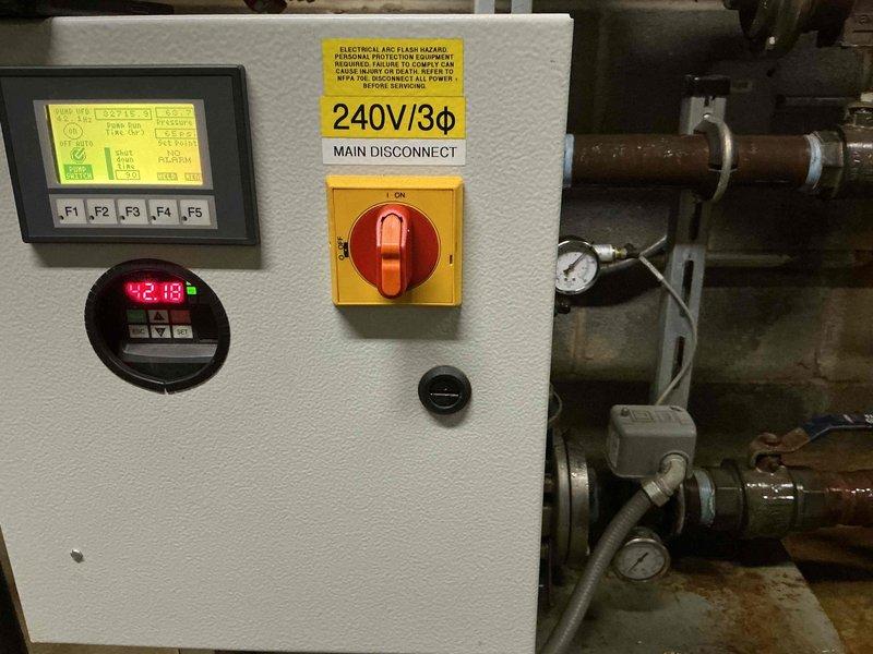 Responded to service call for failed pump on commercial HVAC system. Upon arrival, inspected 240V/3Ø electrical control panel and associated equipment in mechanical room. Verified pump failure through system diagnostics displayed on control interface showing error conditions. Documented existing conditions including digital display readings and electrical disconnect configuration. Captured detailed photographs of control panel assembly, main disconnect switch in ON position, digital meter displaying system parameters, and associated piping infrastructure with pressure gauges and fittings. System monitoring equipment showed operational readings on circular red LED display. Assessed electrical components, lockout/tagout mechanisms, and safety devices for proper functionality. Identified pump replacement required under warranty coverage. Confirmed 240-volt three-phase power supply configuration and verified all safety controls and warning labels present and legible. Documented red fire su