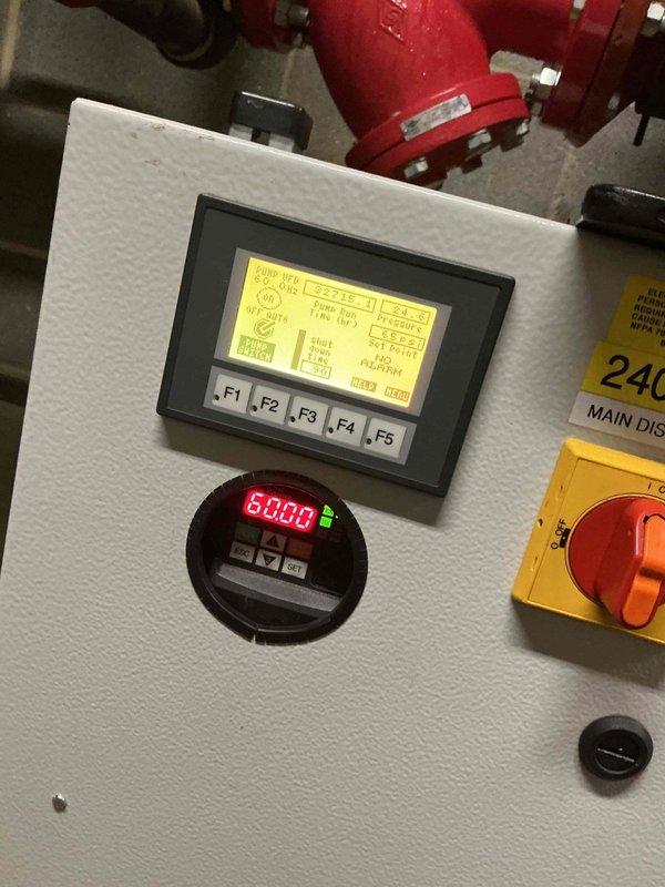 Responded to service call for failed pump on commercial HVAC system. Upon arrival, inspected 240V/3Ø electrical control panel and associated equipment in mechanical room. Verified pump failure through system diagnostics displayed on control interface showing error conditions. Documented existing conditions including digital display readings and electrical disconnect configuration. Captured detailed photographs of control panel assembly, main disconnect switch in ON position, digital meter displaying system parameters, and associated piping infrastructure with pressure gauges and fittings. System monitoring equipment showed operational readings on circular red LED display. Assessed electrical components, lockout/tagout mechanisms, and safety devices for proper functionality. Identified pump replacement required under warranty coverage. Confirmed 240-volt three-phase power supply configuration and verified all safety controls and warning labels present and legible. Documented red fire su