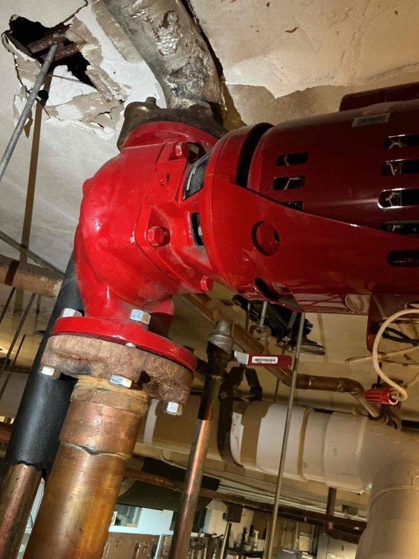 Responded to report of non-operational heating circulation pump serving north side of sanctuary. Upon arrival, inspected red cast iron circulation pump mounted to ceiling in mechanical space. Pump appeared to be recent replacement and potentially under parts warranty per customer communication. Documented pump installation, piping connections including copper supply lines with brass fittings, and overall system configuration. Observed ceiling damage near pump mounting location and noted yellow electrical supply cable with connections. Photographed pump assembly, associated piping, and installation details for warranty documentation and service records.