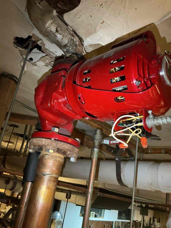 Responded to report of non-operational heating circulation pump serving north side of sanctuary. Upon arrival, inspected red cast iron circulation pump mounted to ceiling in mechanical space. Pump appeared to be recent replacement and potentially under parts warranty per customer communication. Documented pump installation, piping connections including copper supply lines with brass fittings, and overall system configuration. Observed ceiling damage near pump mounting location and noted yellow electrical supply cable with connections. Photographed pump assembly, associated piping, and installation details for warranty documentation and service records.