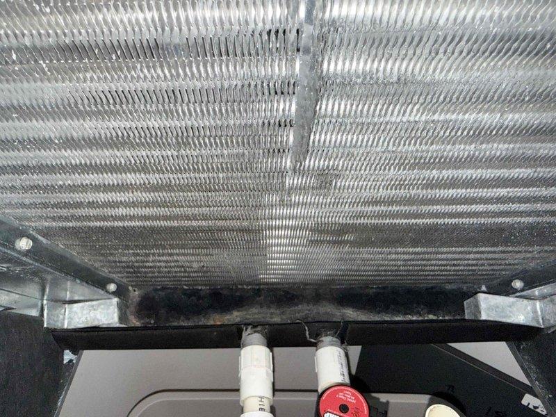 Responded to service call for frozen air conditioning unit. Upon arrival, system had been shut down by homeowner and coil had defrosted. Performed diagnostic inspection of outdoor condensing unit, accessing electrical compartment to examine capacitor, contactor, and wiring connections. Inspected evaporator coil for cleanliness and airflow restrictions. All electrical components tested within normal operating parameters. Documented equipment information and captured photos of unit's internal components and coil assembly for service records.