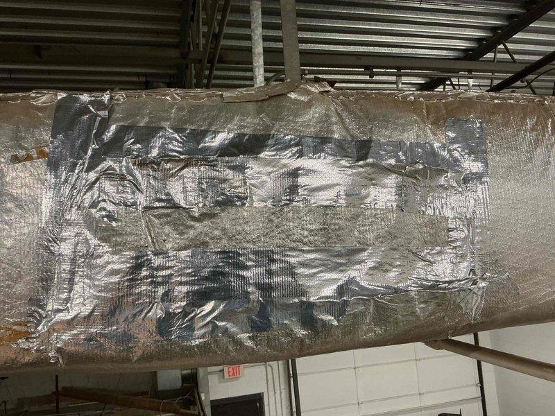 Responded to commercial HVAC ductwork repair request in ceiling plenum space. Upon inspection, found extensive deterioration of reflective insulation wrap on horizontal duct run, with multiple tears, holes, and compromised sections exposing underlying ductwork. Utilized sheet metal to patch damaged areas and secure structural integrity of duct system. Removed deteriorated insulation sections and re-wrapped ductwork with new reflective insulation material, ensuring proper coverage and sealing to maintain thermal efficiency and prevent energy loss. Completed repairs to restore duct insulation system to proper operating condition.
