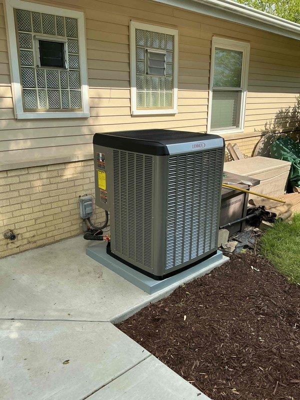 Completed installation of Lennox air conditioning condenser unit on new concrete pad adjacent to residential structure. System mounted on level concrete base with proper clearances maintained from building exterior and landscaping. All electrical connections completed including control boards, transformers, and wiring harnesses with appropriate color-coded conductors. Circuit boards properly secured within equipment cabinet, heat sink and control modules installed, and all manufacturer labels applied. Unit tested and operational upon completion.