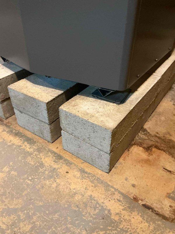 Conducted no-charge warranty service visit and met with Lochinvar factory representative at 9:00 AM to diagnose and address reported banging noise issue from heating equipment. Documented equipment installation and surrounding mechanical room conditions with photographs showing unit mounted on concrete block platform with proper clearances and copper piping connections intact.