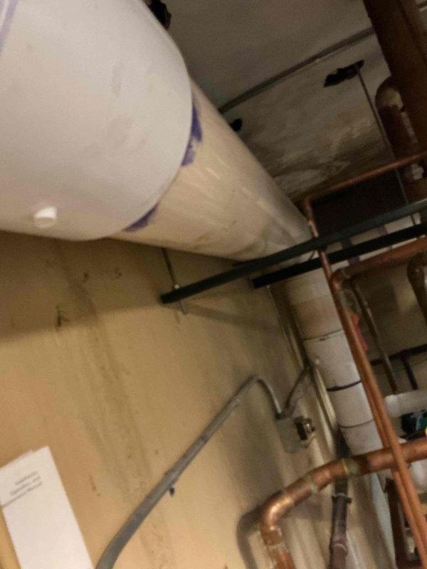Conducted no-charge warranty service visit and met with Lochinvar factory representative at 9:00 AM to diagnose and address reported banging noise issue from heating equipment. Documented equipment installation and surrounding mechanical room conditions with photographs showing unit mounted on concrete block platform with proper clearances and copper piping connections intact.