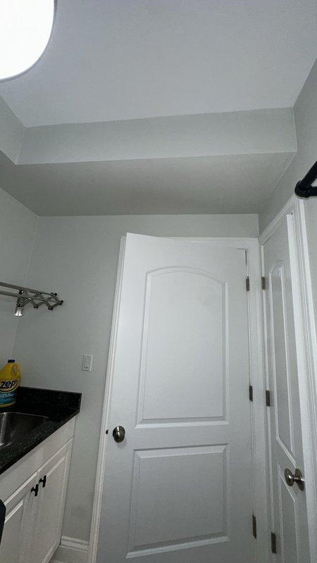 Completed warranty follow-up inspection for previous water damage repair in laundry room area. Assessed quality of trim work and paint application on walls, doors, and ceiling surfaces to verify proper restoration. Documented completed repairs showing professionally finished light gray walls, white trim, crown molding, and door frames with no visible signs of water staining or damage remaining.