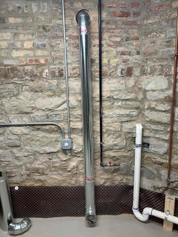 Completed coring operation through basement masonry wall to accommodate dryer vent exhaust system. Installed 4-inch rigid ductwork from wall penetration to termination point near floor level where appliance will be positioned, finishing with 90-degree elbow fitting for proper connection to dryer unit.