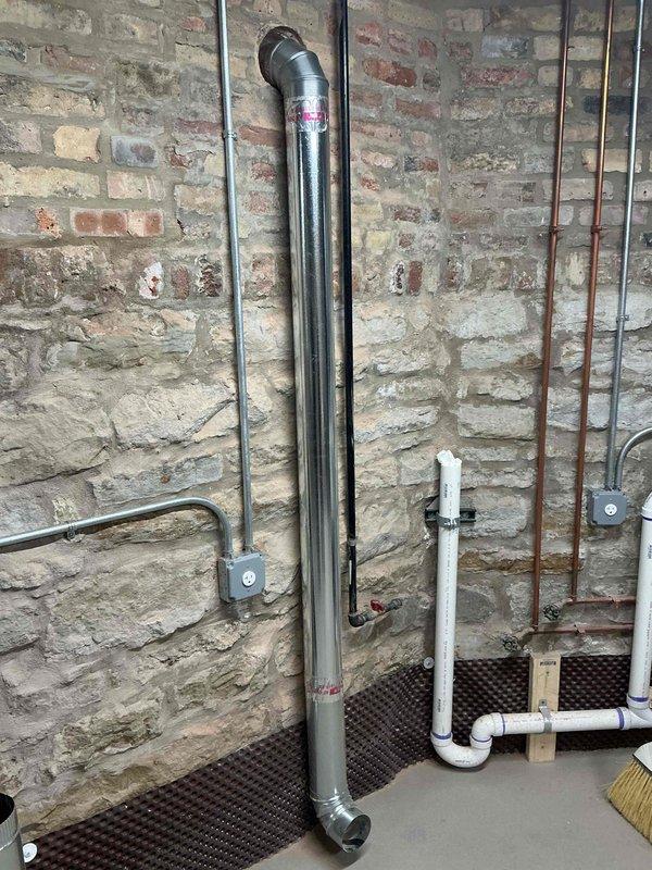 Completed coring operation through basement masonry wall to accommodate dryer vent exhaust system. Installed 4-inch rigid ductwork from wall penetration to termination point near floor level where appliance will be positioned, finishing with 90-degree elbow fitting for proper connection to dryer unit.