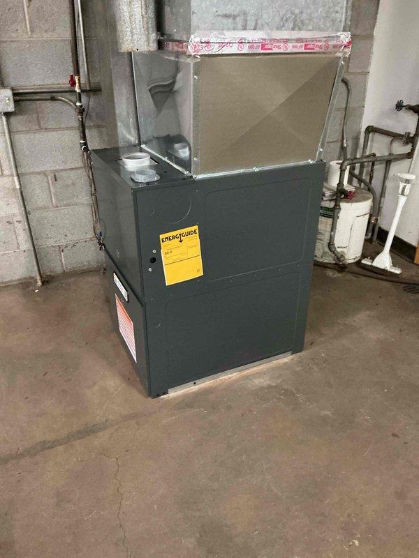 Completed installation of an 80% efficiency gas furnace rated at 100-110,000 BTU in a commercial basement utility room. Unit was positioned on concrete floor against masonry block wall, with all ductwork connections, venting, and gas supply lines properly installed and secured per manufacturer specifications and local building codes.