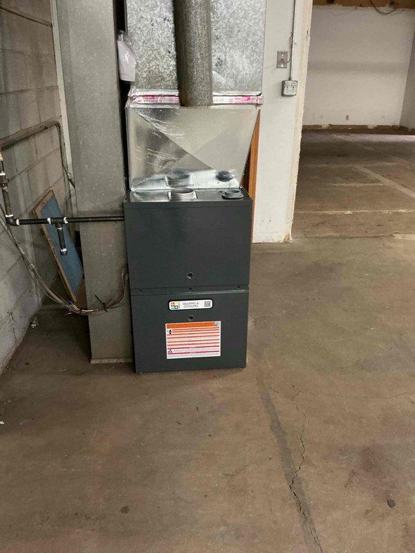 Completed installation of an 80% efficiency gas furnace rated at 100-110,000 BTU in a commercial basement utility room. Unit was positioned on concrete floor against masonry block wall, with all ductwork connections, venting, and gas supply lines properly installed and secured per manufacturer specifications and local building codes.