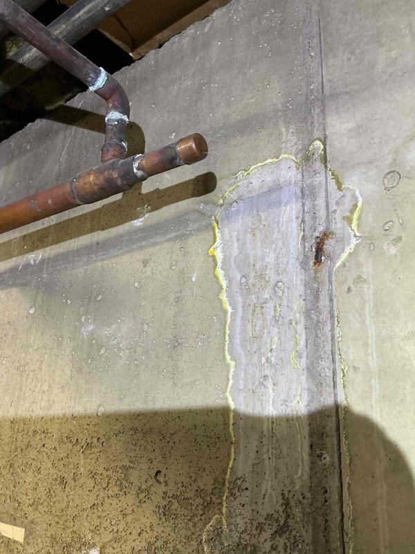 Responded to commercial water leak in boiler room. Upon arrival, diagnosed active leak on half-inch copper pipe penetrating concrete wall, evidenced by significant moisture damage, efflorescence staining, and vertical water streaking on wall surface. Documented extensive frost and ice buildup on copper piping and surrounding insulated surfaces, indicating ongoing moisture intrusion and temperature differential issues. Photographed corrosion on copper connections, condensation patterns, and compromised insulation integrity for repair authorization.