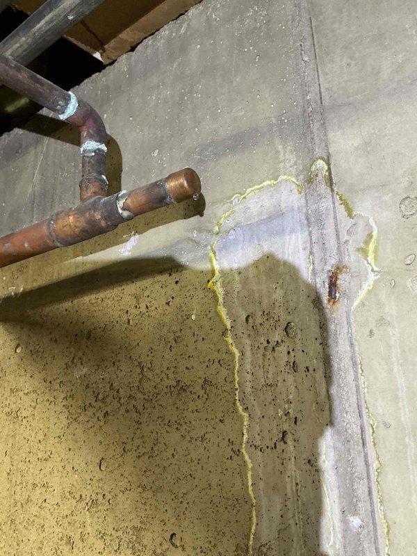 Responded to commercial water leak in boiler room. Upon arrival, diagnosed active leak on half-inch copper pipe penetrating concrete wall, evidenced by significant moisture damage, efflorescence staining, and vertical water streaking on wall surface. Documented extensive frost and ice buildup on copper piping and surrounding insulated surfaces, indicating ongoing moisture intrusion and temperature differential issues. Photographed corrosion on copper connections, condensation patterns, and compromised insulation integrity for repair authorization.